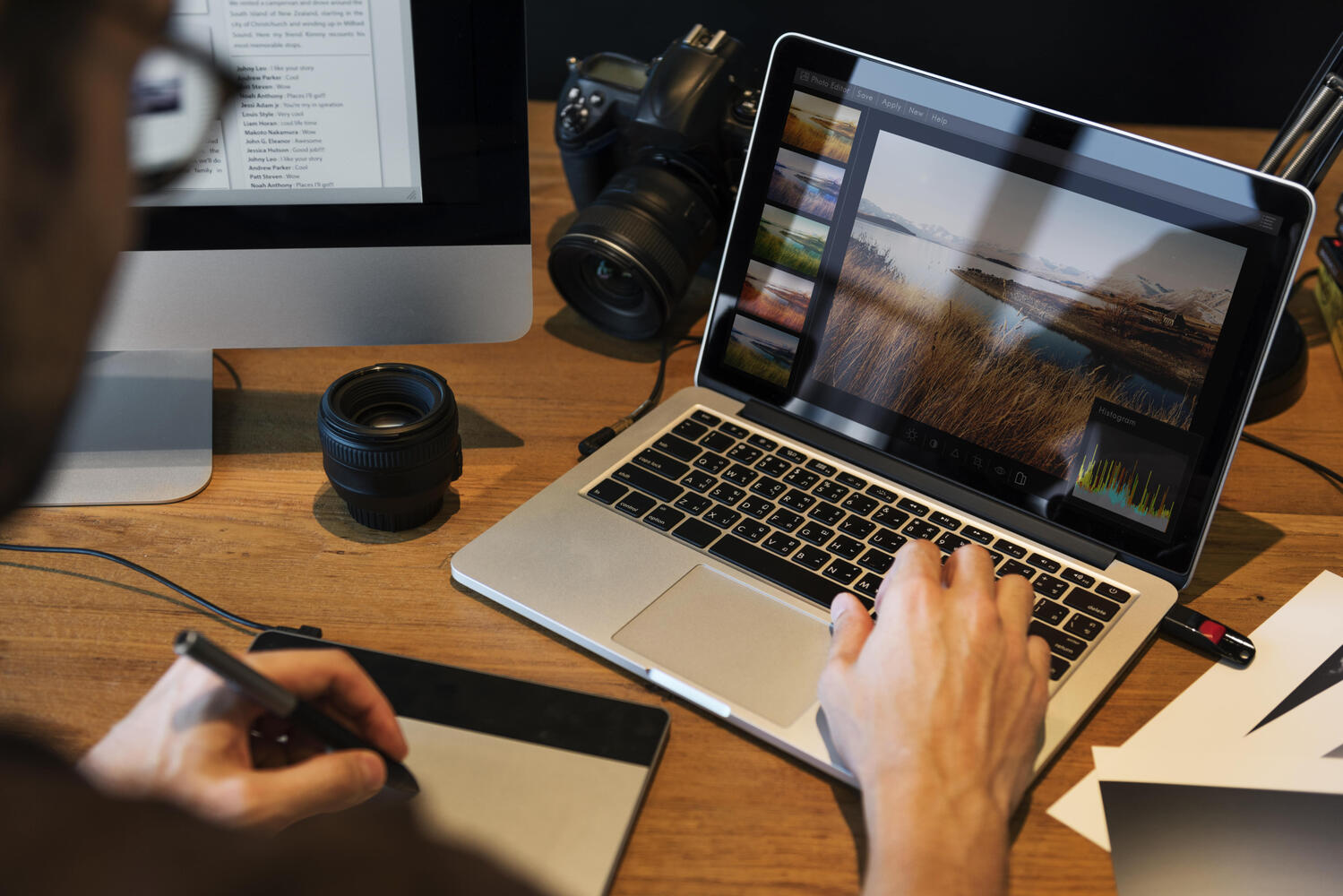Video bearbeiten Schlauer Typ sitzt an einem Schreibtisch mit Kamera, MacBook und Handy auf dem Tisch. Er bearbeitet Videoaufnahmen, die er für einen Kunden gedreht hat.